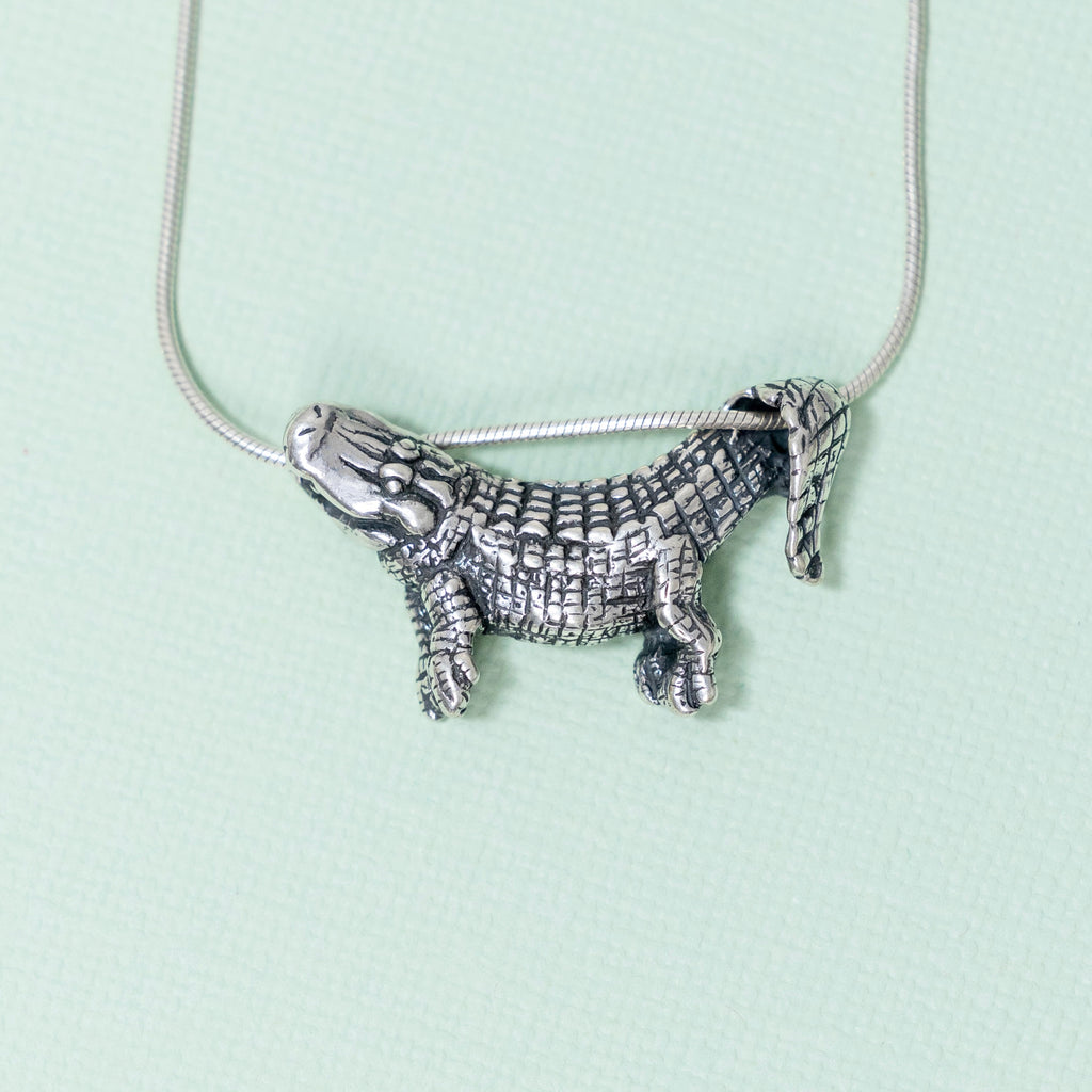 A sterling silver pendant in the shape of an alligator designed to dangle from a chain, with focus on the pendant against a light background.
