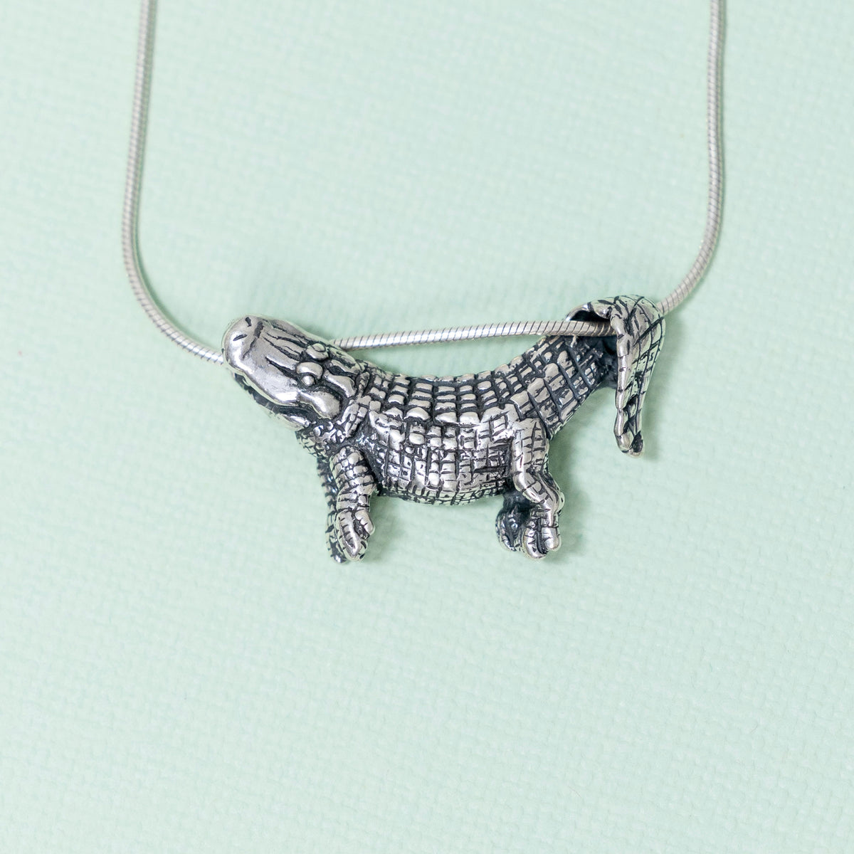 A sterling silver pendant in the shape of an alligator designed to dangle from a chain, with focus on the pendant against a light background.