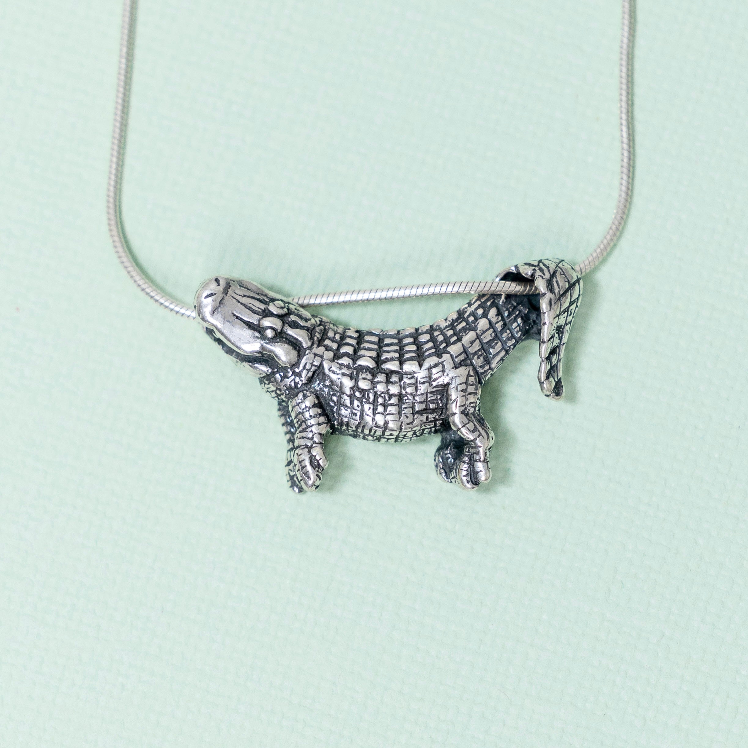 A sterling silver pendant in the shape of an alligator designed to dangle from a chain, with focus on the pendant against a light background.