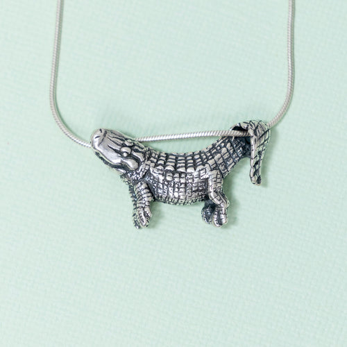 A sterling silver pendant in the shape of an alligator designed to dangle from a chain, with focus on the pendant against a light background.