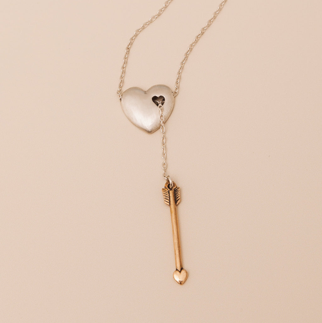 Close-up of sterling silver heart necklace pierced with bronze arrow