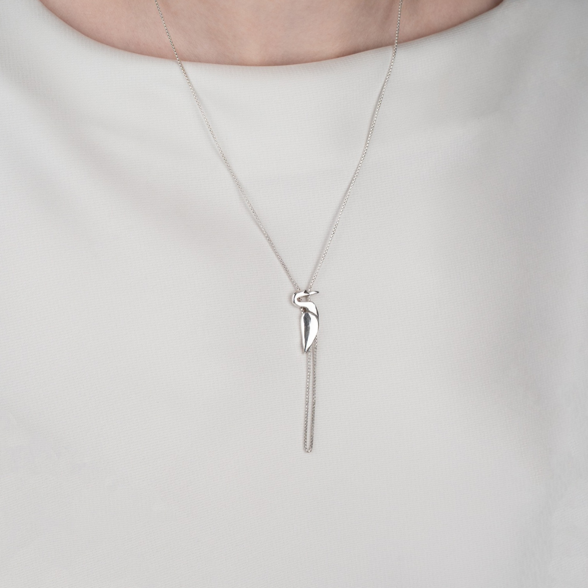 Sterling silver Egret Necklace styled with a white top, showcasing its elegant bird silhouette and long dangling chain.
