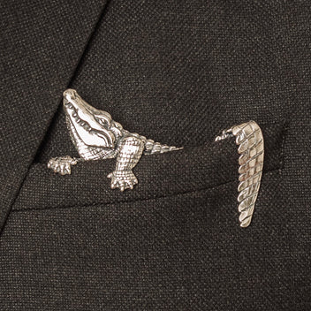 A handcrafted sterling silver pocket square with a carved alligator design inserted into a jacket pocket, standing upright.