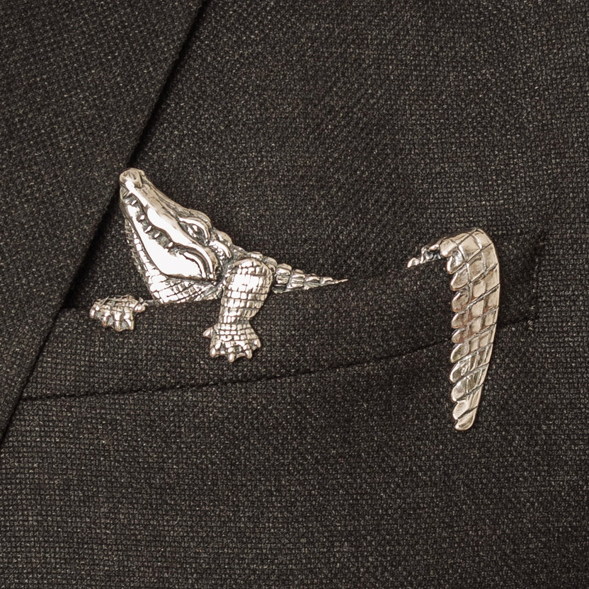 A handcrafted sterling silver pocket square with a carved alligator design inserted into a jacket pocket, standing upright.