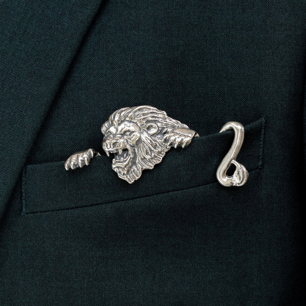 A sterling silver pocket square with a carved lion design inserted into a black jacket pocket.