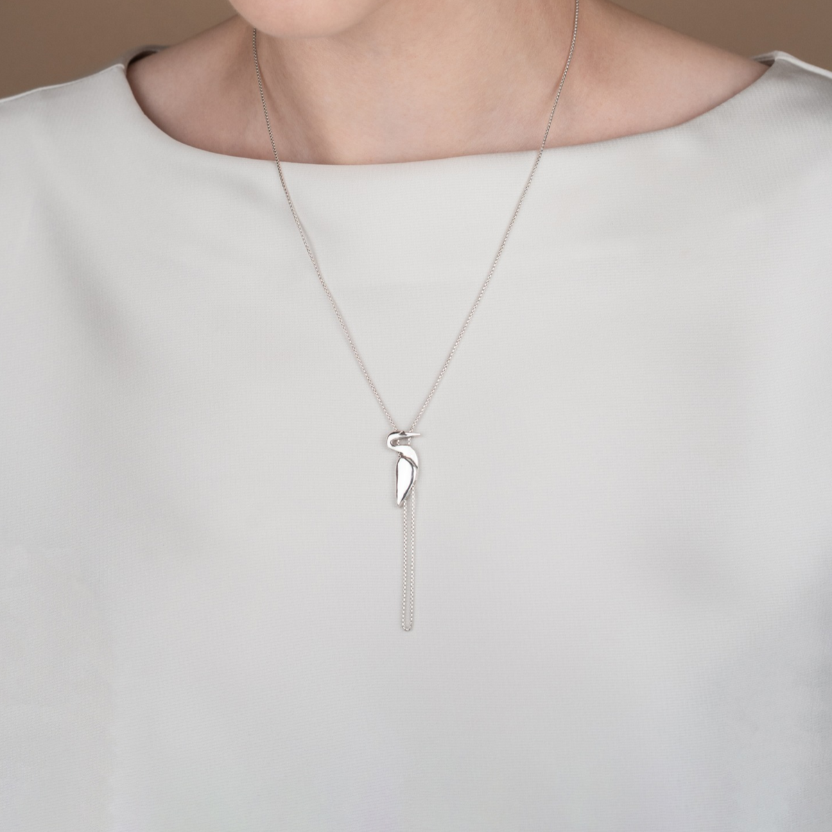 Model wearing the sterling silver Egret Necklace by Jose Balli Jewelry, showing the necklace's length and sculptural bird pendant.