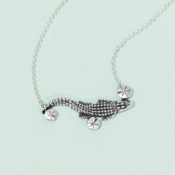 A sterling silver necklace featuring a detailed alligator charm swimming through lily pads, attached to a chain.