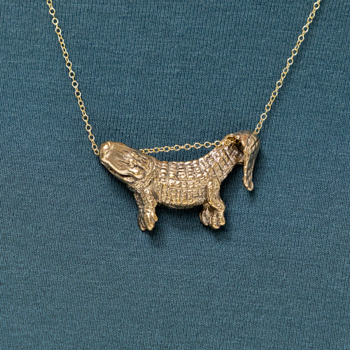A bronze dangling alligator pendant on a chain, displayed against a blue background.