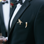 Close-up of a black tuxedo with a gold alligator brooch on the lapel.