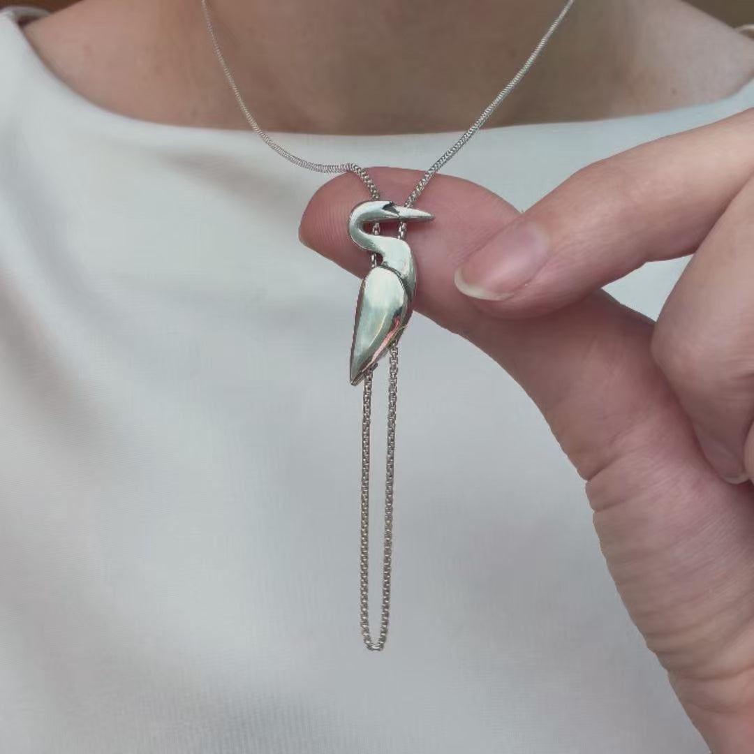 Close-up video of the sterling silver Egret Necklace being worn and displayed, highlighting the sculptural pendant and dangling chain.