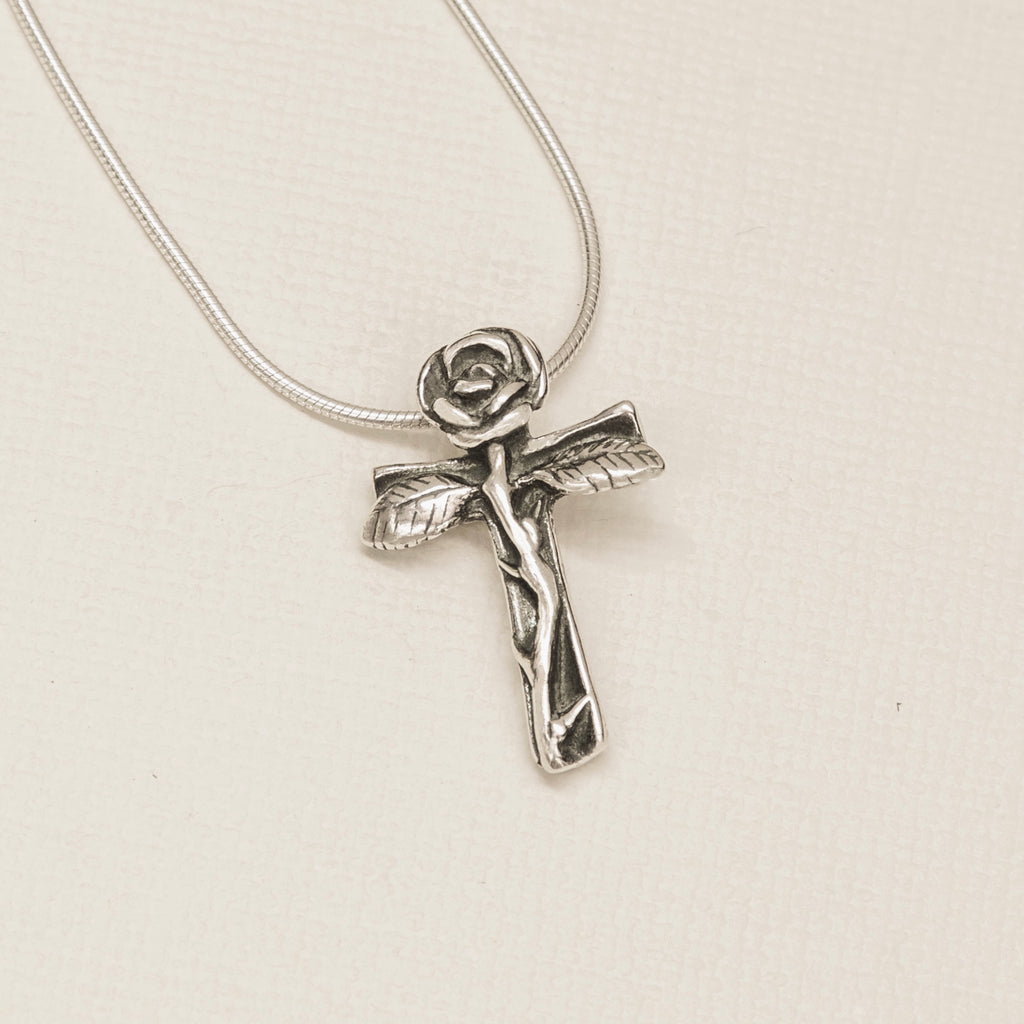 Sterling silver rose cross pendant on beige flat lay detail close up 