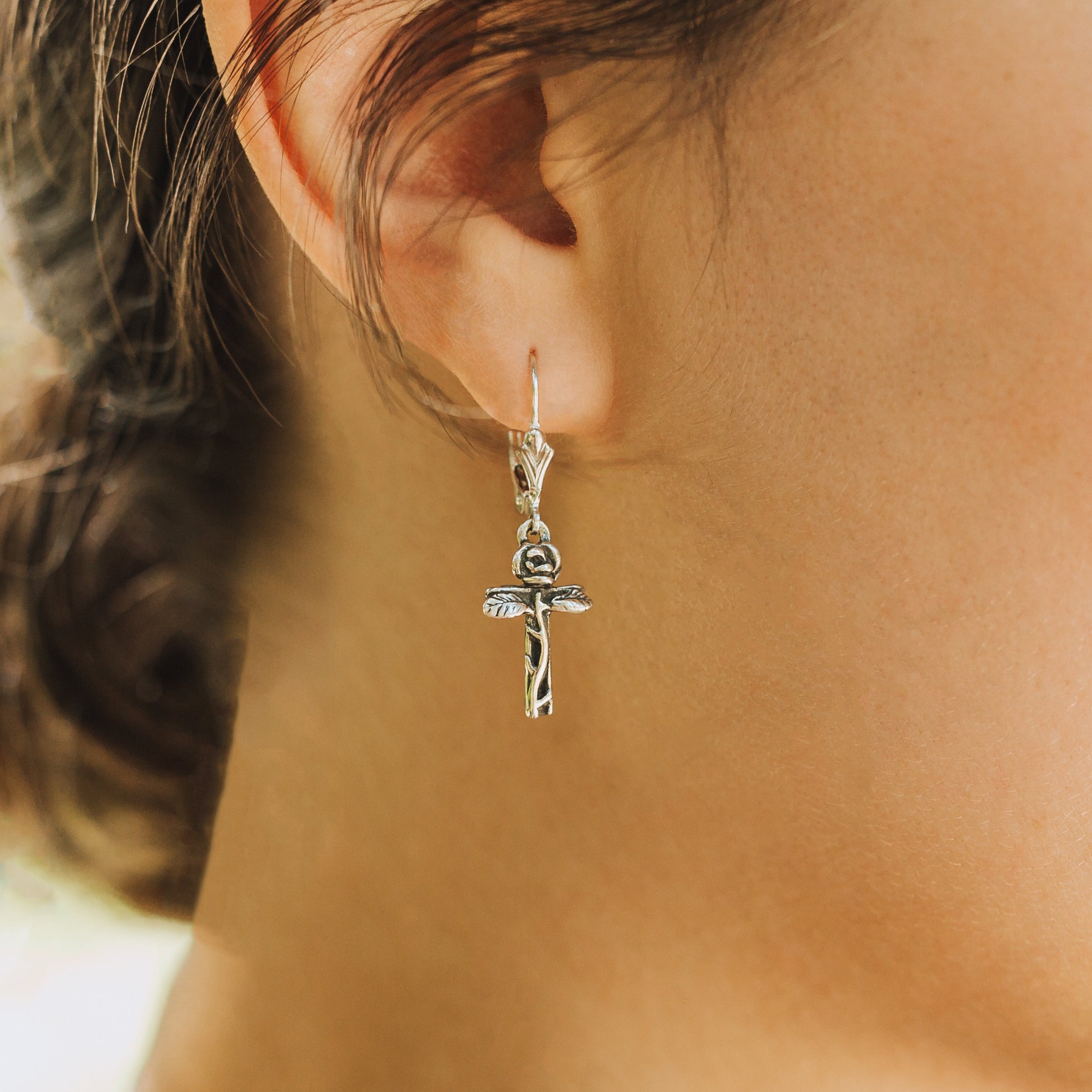 petite rose cross earrings worn on ear close up