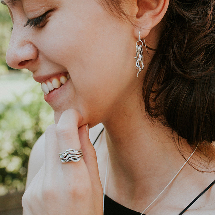 Woman smiling while wearing a silver Spanish Moss ring and matching earrings.