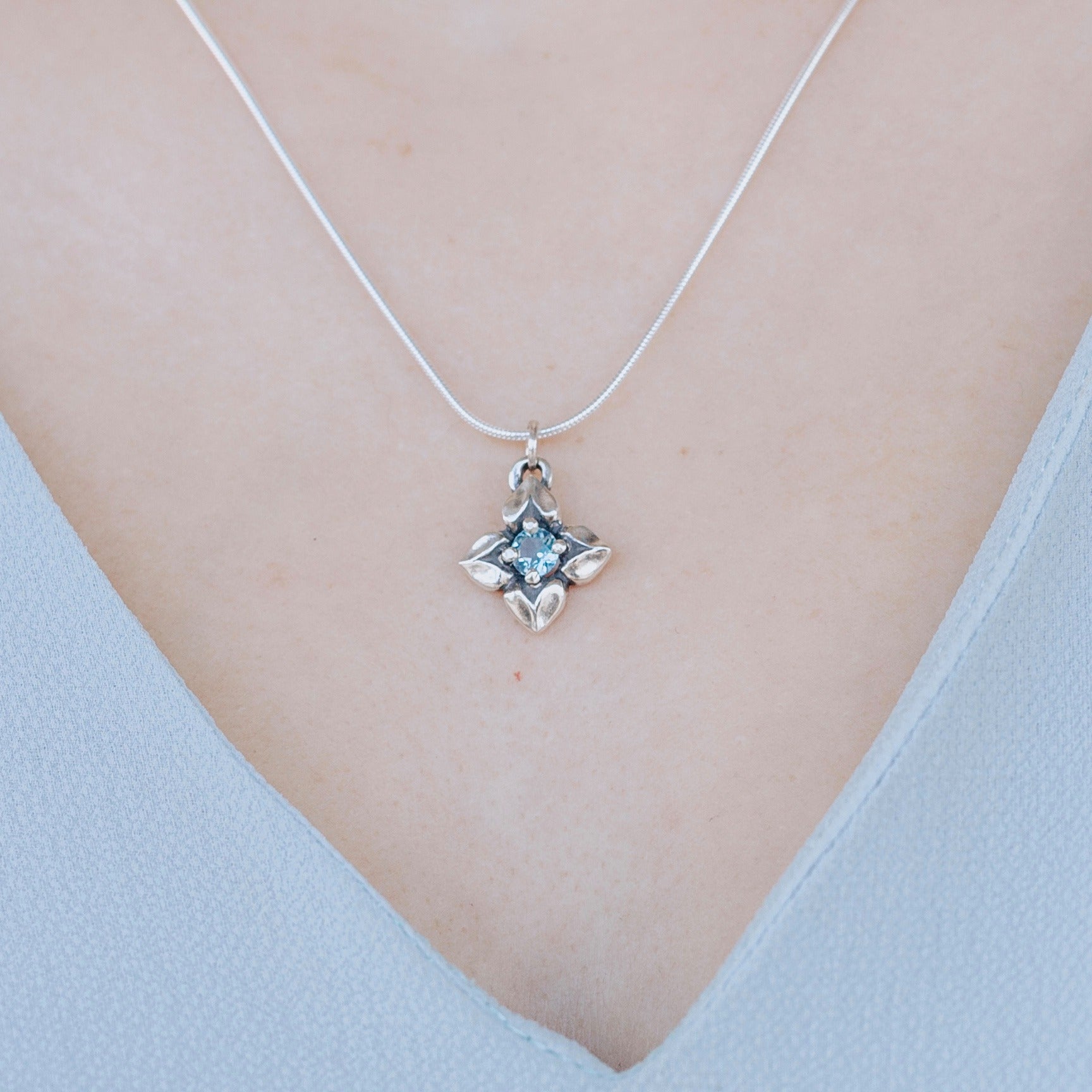 woman wearing blue topaz flower pendant in sterling silver floral design