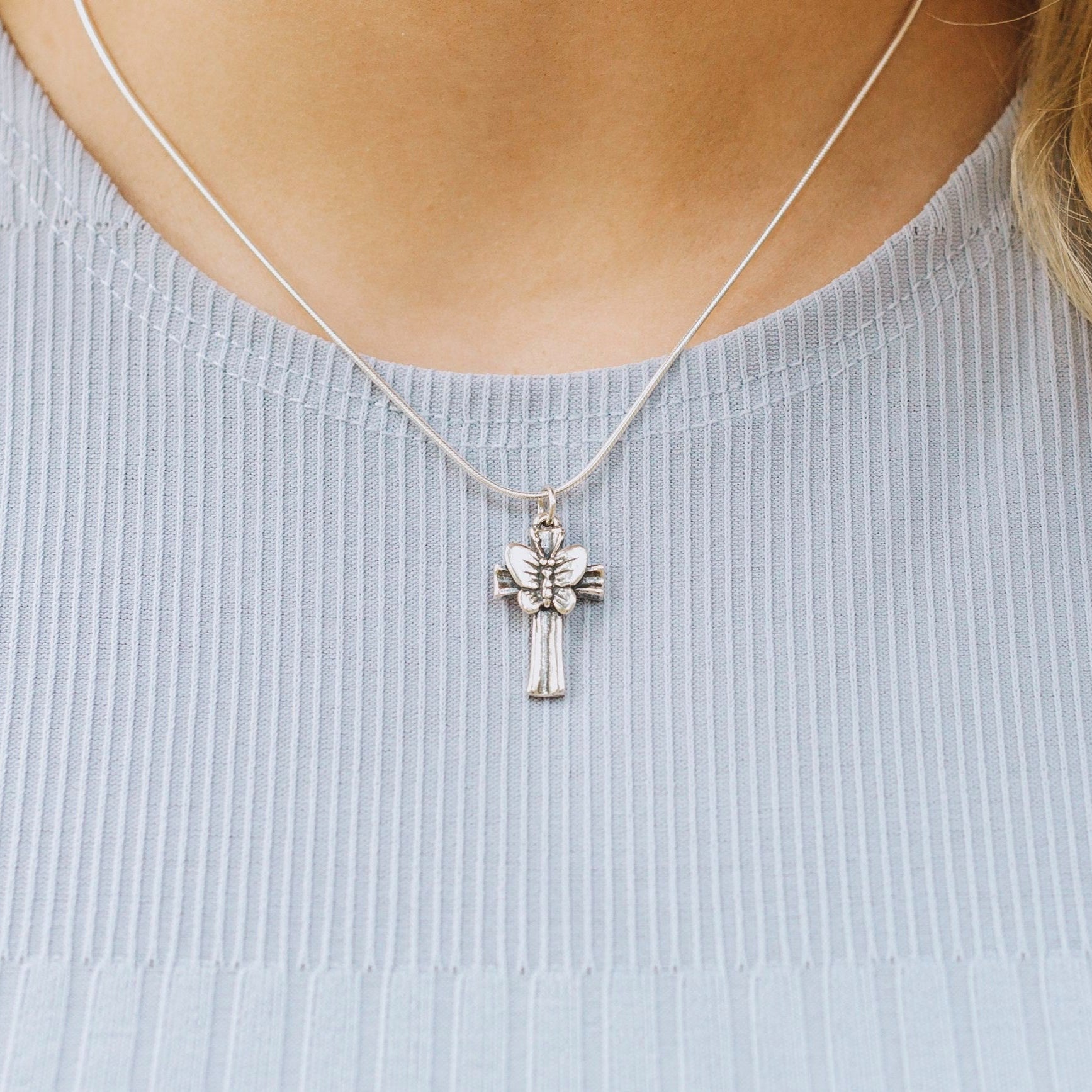 Close-up of butterfly cross pendant necklace worn