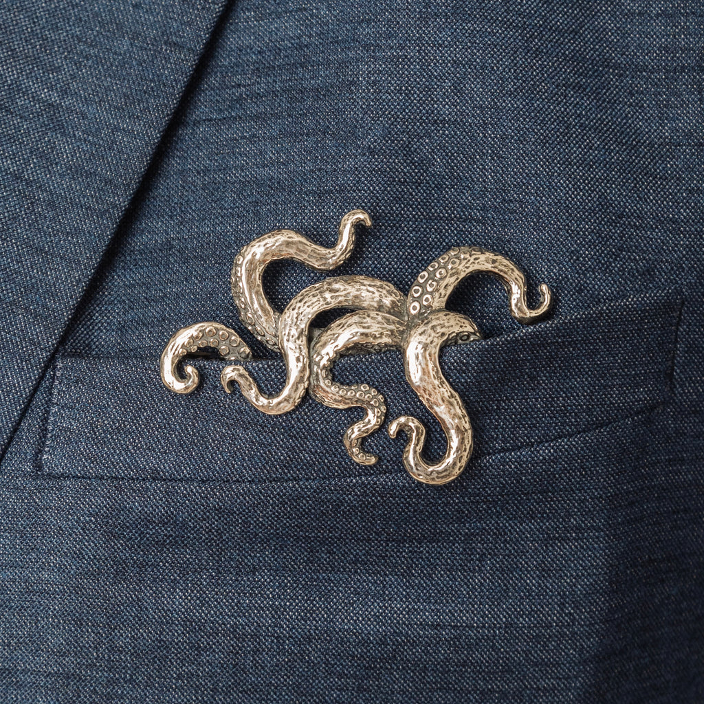 A silver-colored, hand-carved octopus (Kraken) pocket square insert protruding from a suit jacket pocket.
