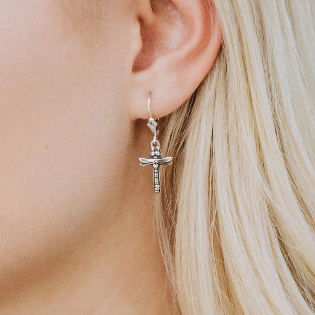 Close-up of petite dragonfly cross earrings worn on ear