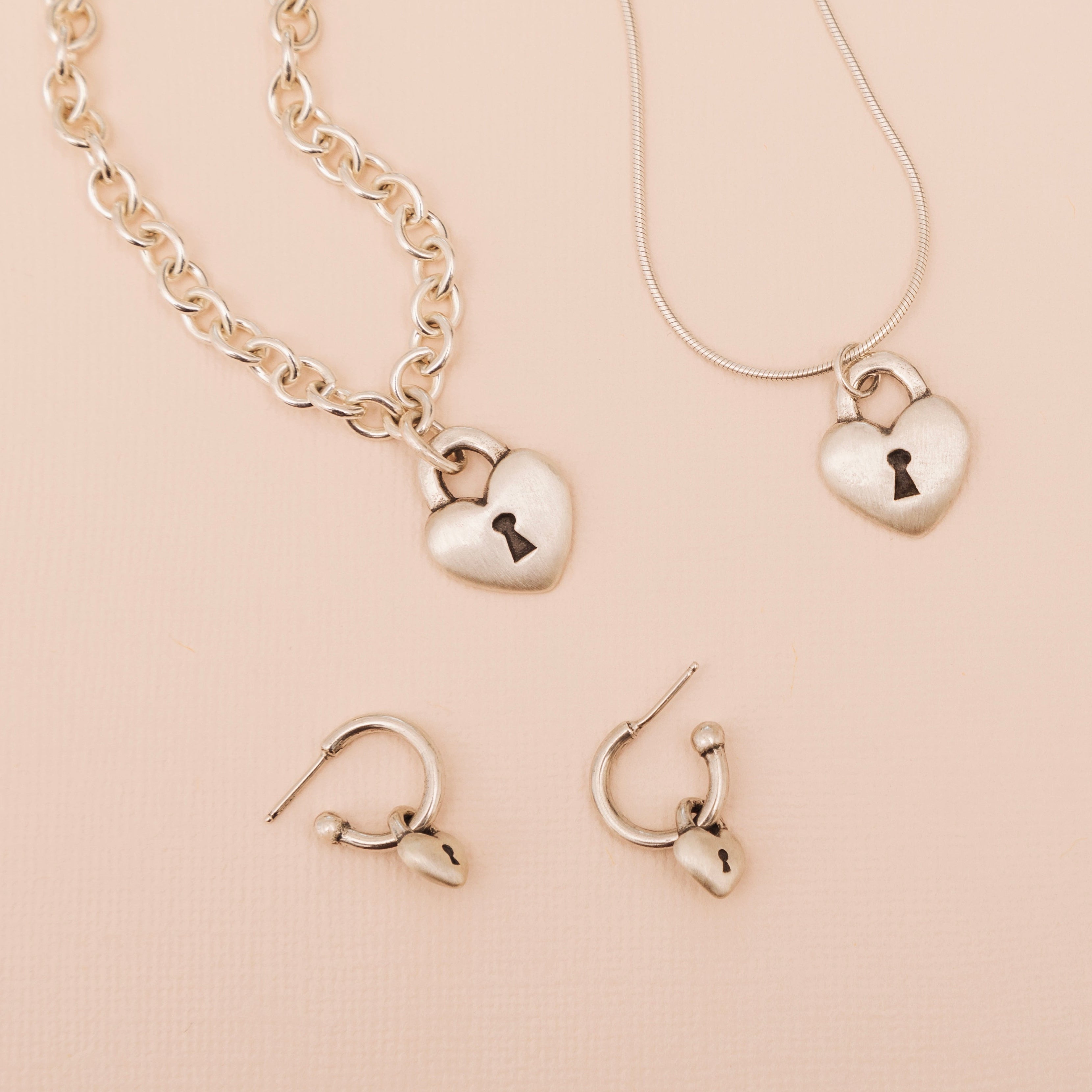 Sterling silver heart love lock necklace styled with matching jewelry on soft peach background